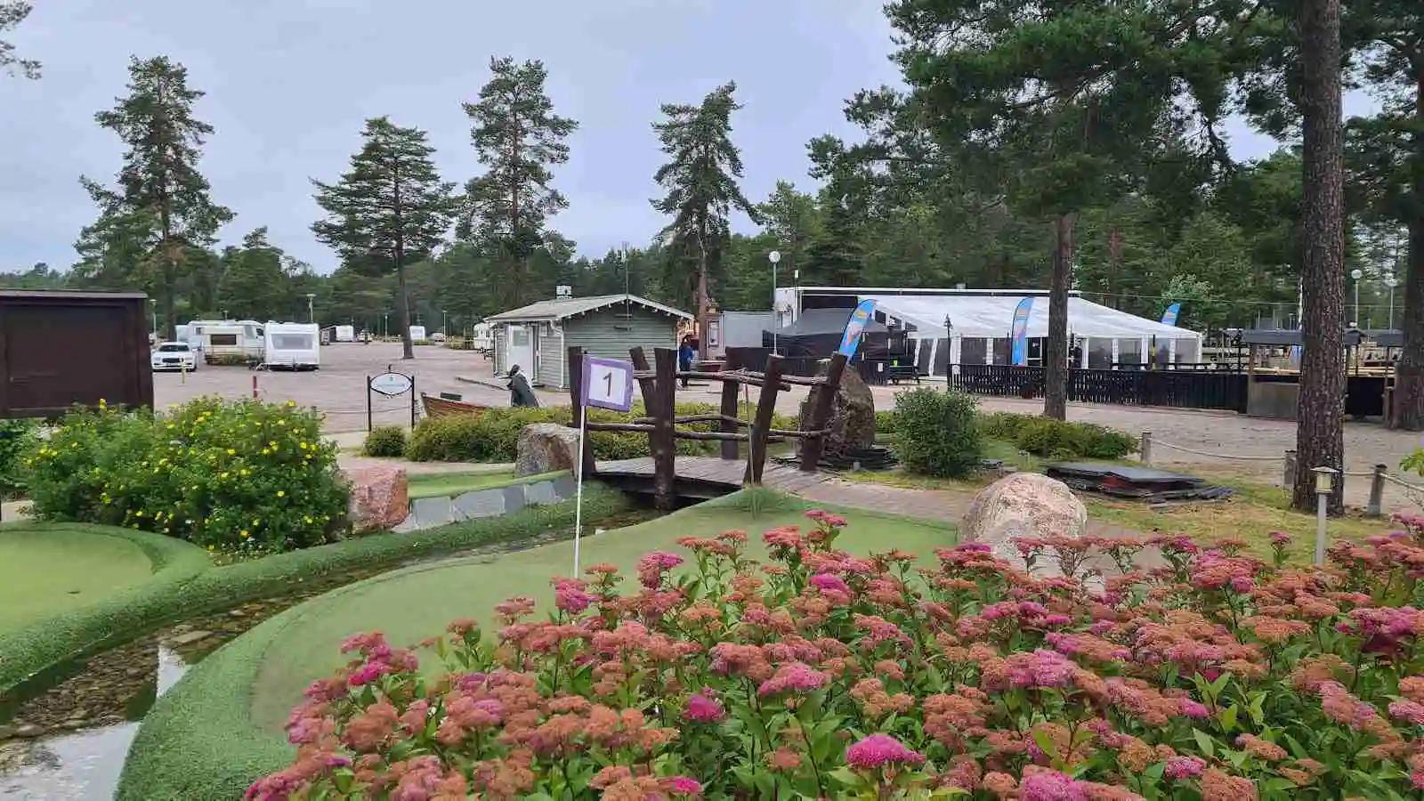 En grönskande campingplats med välskött trädgård och landskapsplanering. Gångväg och viloplats omgiven av växter i parkliknande miljö.