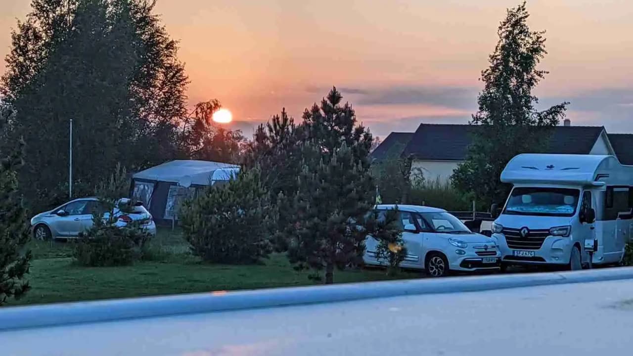 En husbil parkerad vid Fredriksbergs kursgård-camping vid skymningen, speglar och bakljus synliga, omgiven av natur.