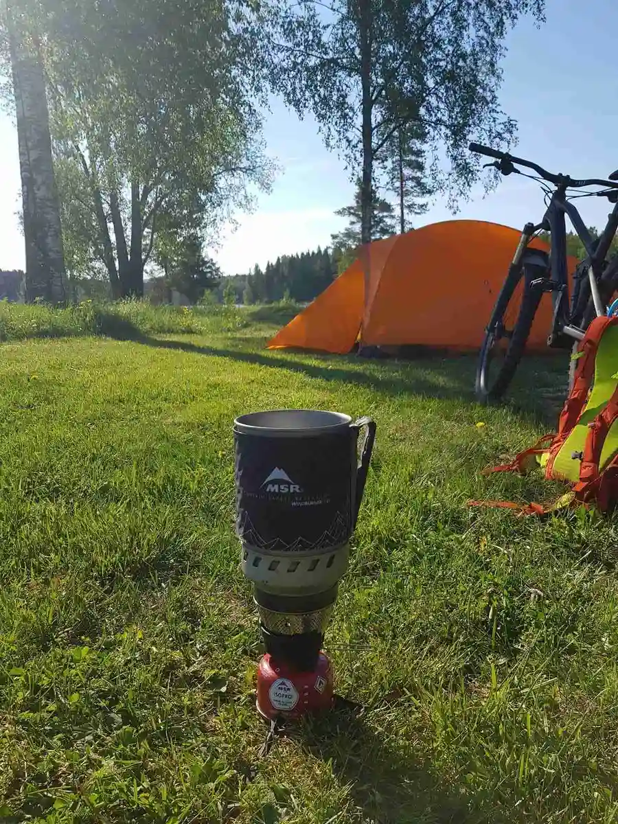 Bild av en grönskande gräsmatta vid Sörälgens camping med tält och husvagnar i bakgrunden, omgiven av lummiga träd.