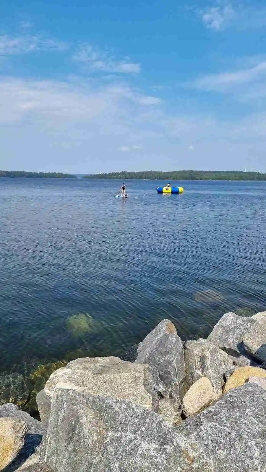 En vacker somrig utsikt över en klarblå sjö vid camping Tiveden, med en vidsträckt horisont under en molnfri himmel, perfekt för avkopplande utomhusaktiviteter och rekreation.