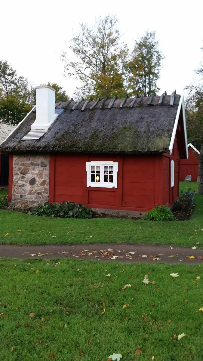 En mysig stuga med träfasad och tak beläget på Elfdalens camping, omgiven av grönskande gräs och buskar i en lantlig miljö.