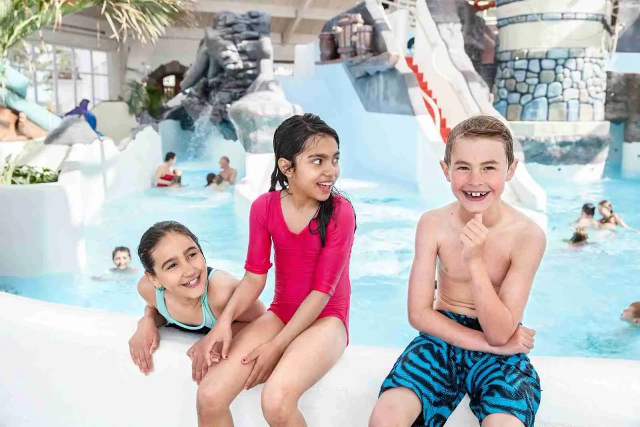 En glad familj badar och leker i en vattenpark på Västervik Resort, med barn i baddräkter som njuter av semestern i poolen.