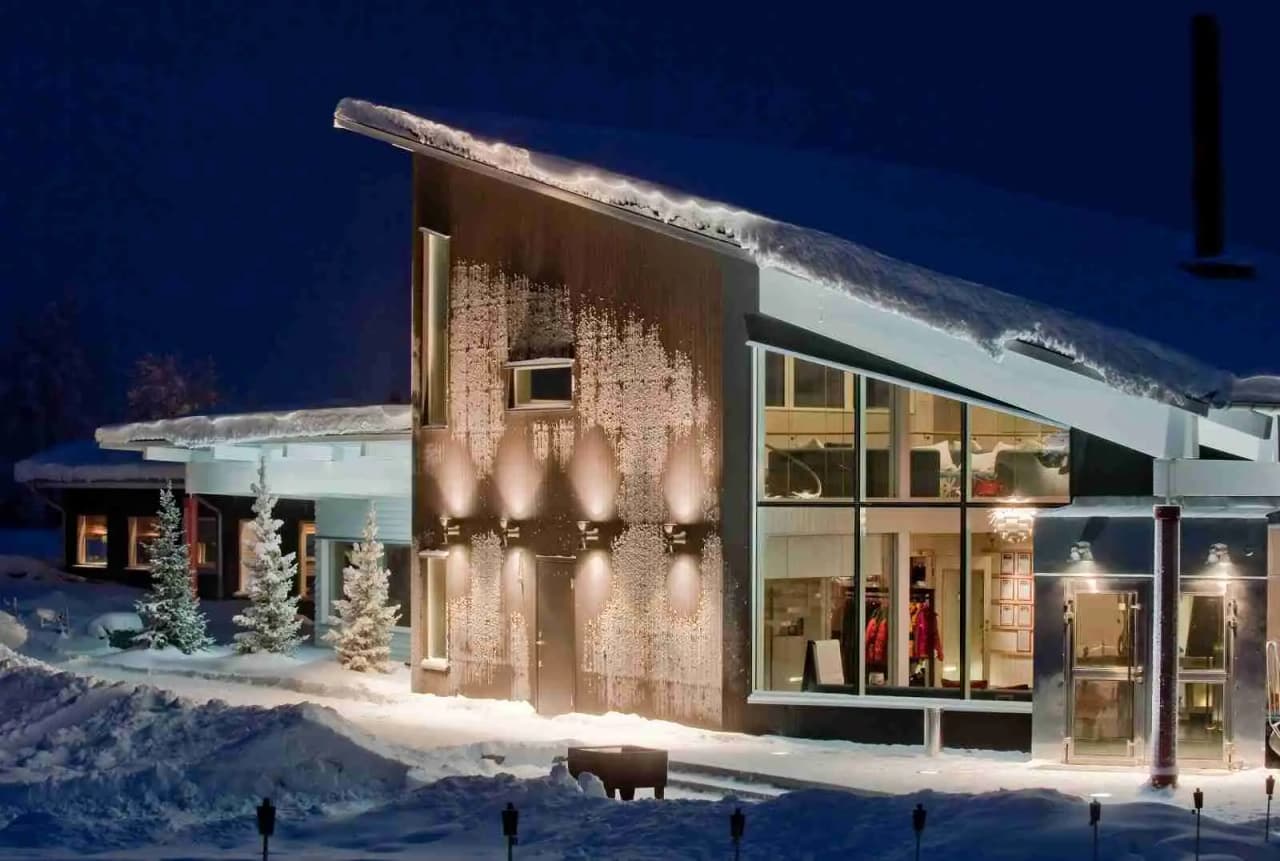 En snötäckt stuga vid Camp Ripan, upplyst i nattens mörker, omgiven av vinterklädda barrträd.