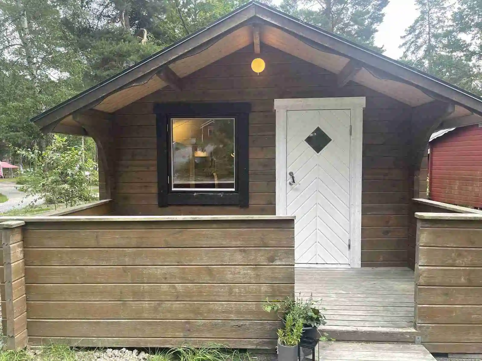 Bild på en trästuga med en enkel dörr, omgiven av skoglig miljö på Waxholms camping.