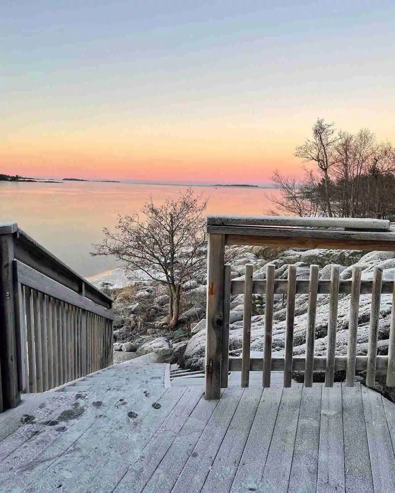 En vintervy över kust och hamn i Ängskär vid skymning eller gryning, med snö och frost på marken, och en brygga som leder ut mot horisonten under en kylig himmel.