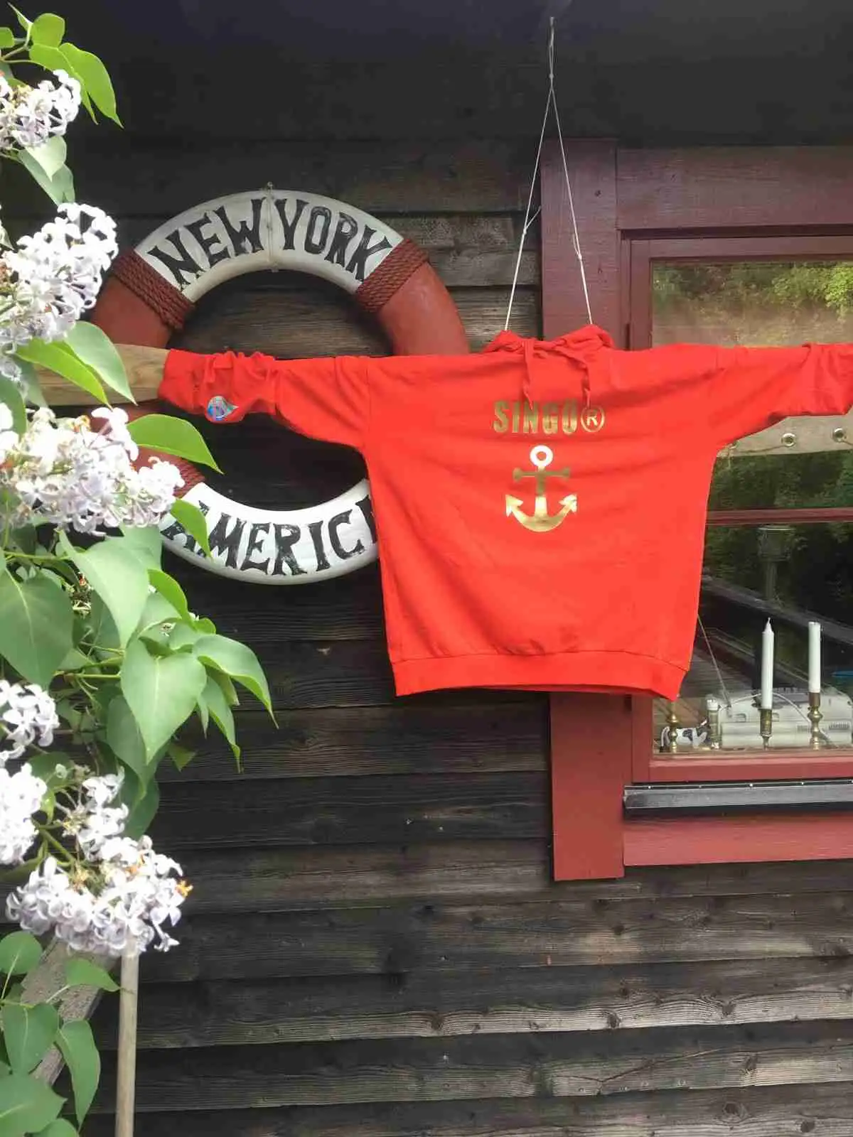 En person iförd en orange aktivitetströja står på ett trädäck omgivet av blommande pelargoner vid Norrtälje camping.