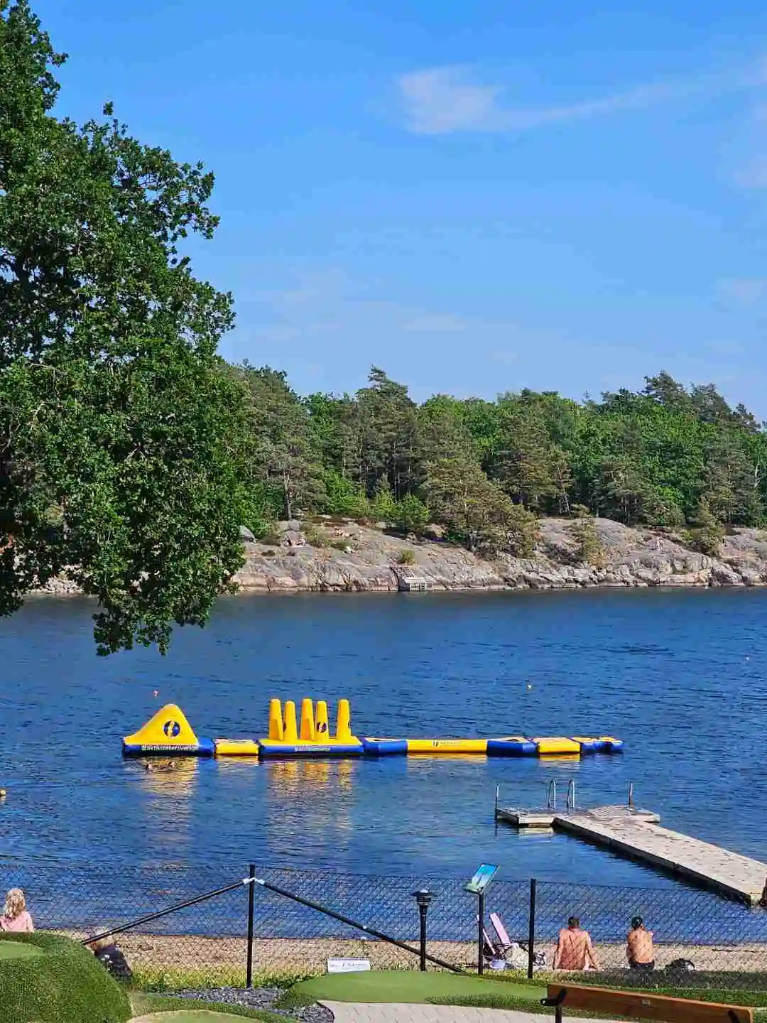 En somrig campingplats vid en sjö med båtar i vattnet. Området inbjuder till rekreation med fokus på avkoppling och semesteraktiviteter.