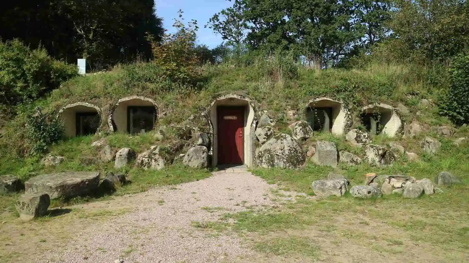 En bild av den pittoreska Grottbyns camping, där charmiga stugor i stenruiner-stil står mot en lummig bakgrund, vilket ger platsen en tidlös och äventyrlig atmosfär.