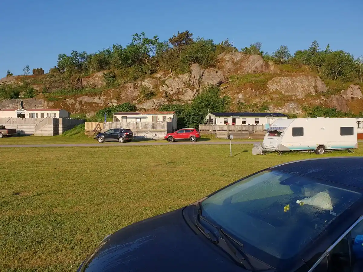 En parkeringsplats på Örns camping med olika fordon, inklusive en husbil och en SUV, omgivna av grönska.