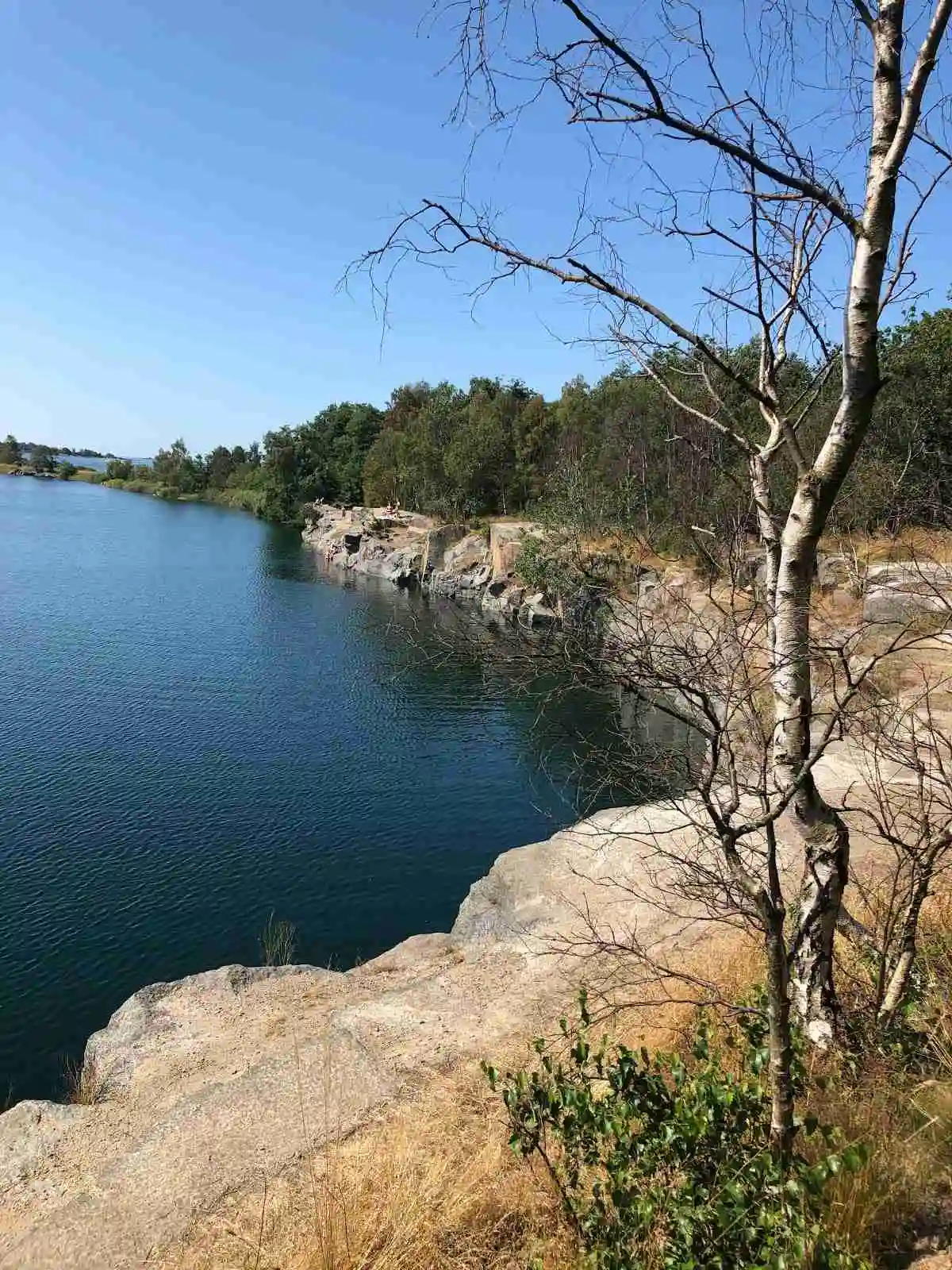 Vy över Ronneby havscamping med kustlinje och vatten i förgrunden; stenar och frodig omgivning skapar en inbjudande naturlig atmosfär.