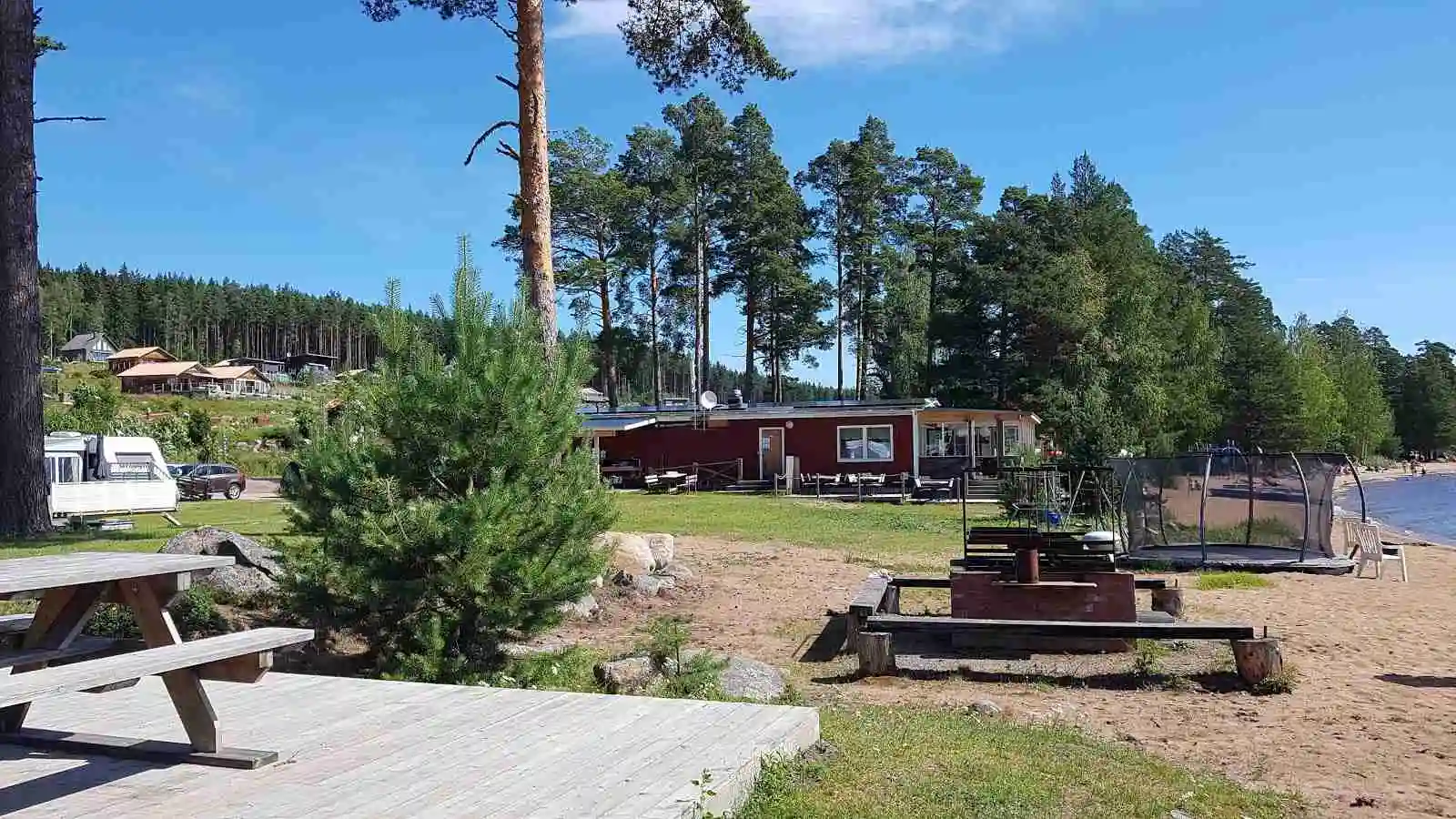 En idyllisk campingplats med en röd stuga bland höga tallar och grönskande barrträd, norra dellen familjecamping, som erbjuder avkopplande boende i naturskön omgivning.