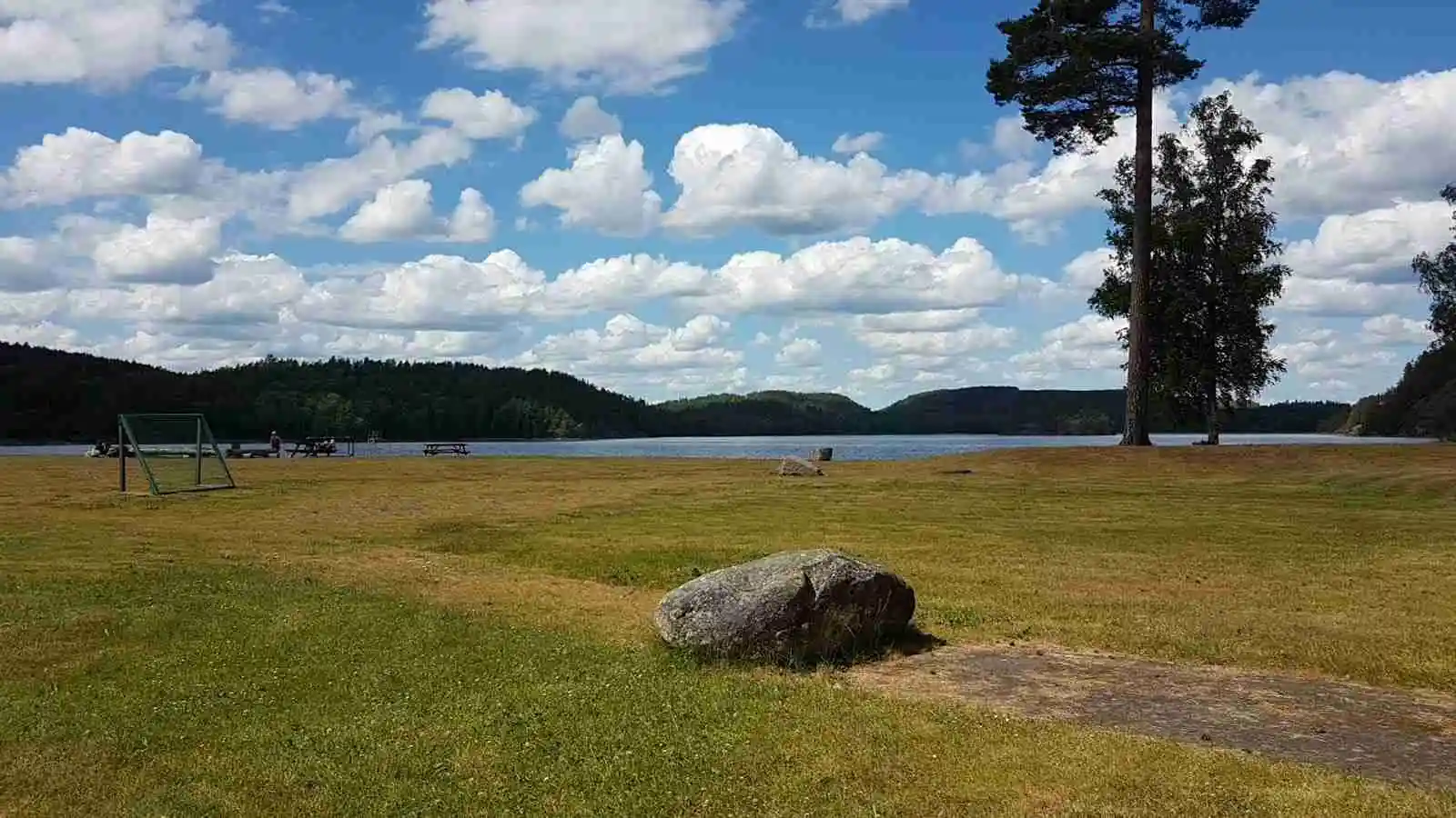 En fridfull sjö omgiven av grönskande ängar under en himmel med vita moln vid Pinnarp Camping.