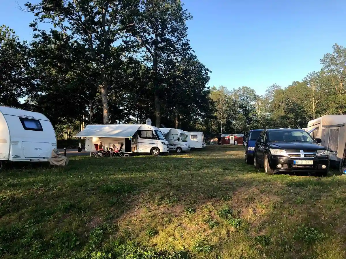 En campingplats på Alsterbro med flera parkerade husbilar och bilar omgivna av träd i en naturskön miljö.