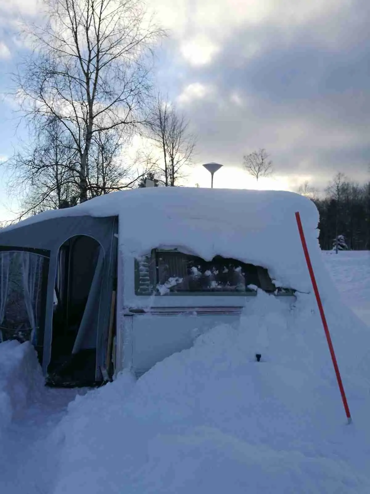 Bild av Hede Camping under vintern, täckt av snö och is. En husvagn syns omgiven av ett vinterlandskap med frost och fallande snöflingor.